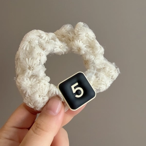 Detail of white lace hair scrunchie with floral texture and black number 5 tag