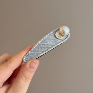 Detail of grey fabric hair clip with white faux pearl and golden circular metal charm