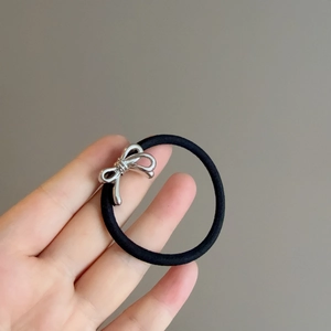 Close-up of black elastic hair tie featuring a shiny silver metal bow charm