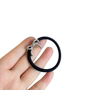 Minimalist black elastic hair tie featuring a polished silver metal bow pendant