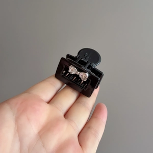 Detail of small black hair claw clip with sparkling rhinestone bow held in hand