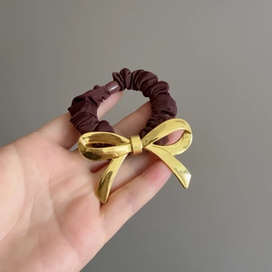Dettaglio dell'elastico marrone scuro con fiocco in metallo dorato lucido e chic