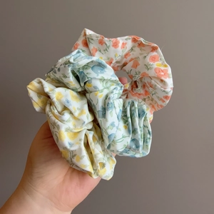 Close-up of three floral print scrunchies in yellow, blue and pink soft fabric