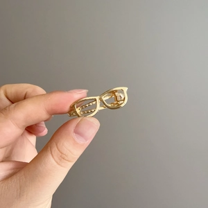 Détail d'une pince à cheveux en métal doré en forme de monture de lunettes unique