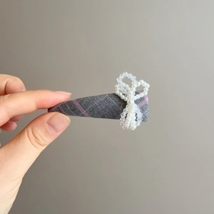 Détail macro d'une barrette en tissu écossais gris avec un nœud délicat en perles blanches