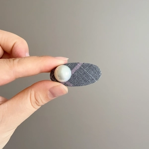 Détail de la pince à cheveux en tissu écossais gris avec une perle blanche élégante