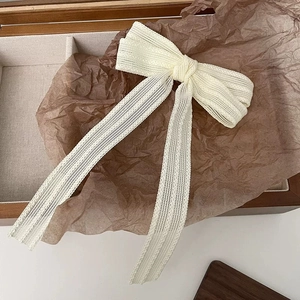 Detailed close-up of cream lace bow hair clip with ribbons on vintage wooden display