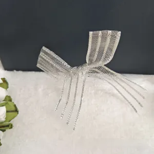 Detail showing silver mesh bow hair clip with flowing metallic tassels on a soft surface