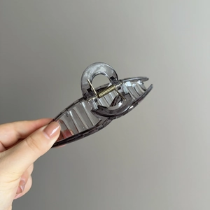Pince à cheveux minimaliste grise translucide avec ressort en métal tenue à la main