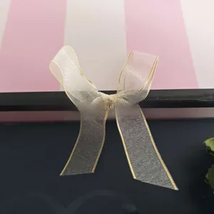 Detailed close-up of a white organza bow hair clip with elegant gold silk embroidered edges