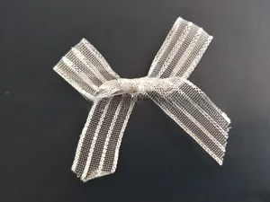 Close-up of white mesh bow hair clip with silver glitter stripes on dark background
