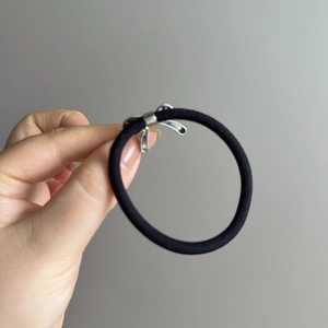 Élastique à cheveux noir avec nœud en métal argenté poli sur fond gris neutre