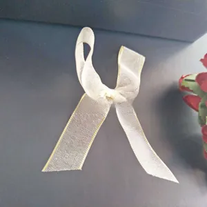 Detail showing cream organza bow hair clip with gold stitching on dark grey surface