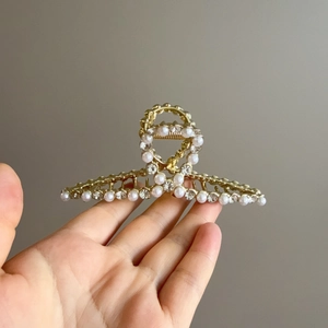 Détail d'une pince à cheveux dorée ornée de perles doubles et de strass étincelants