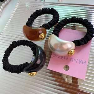 Close-up of three hair ties with amber, pearl and black beads on elastic fabric