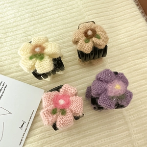 Dettaglio di quattro mollette per capelli a fiori in maglia color crema rosa e viola