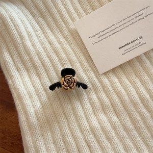 Elegant black hair claw with a gold 3D rose accent on soft white knitted fabric