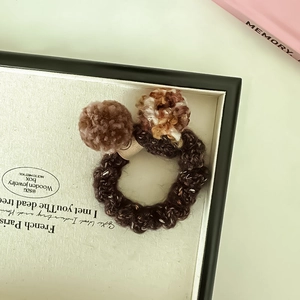 Détail d'un chouchou en maille avec pompons en peluche marron pour coiffure douce