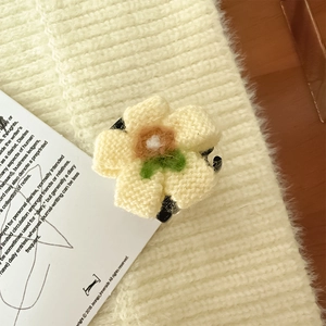Dettaglio della pinza per capelli a fiore lavorato a maglia giallo con centro arancione e foglie