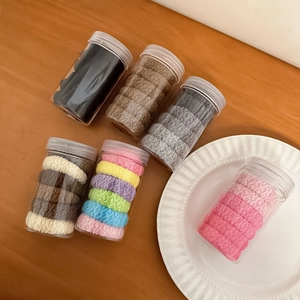 Thick elastic hair ties set in clear jars on wood table with a white ceramic plate