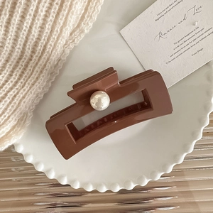 Elegante molletta per capelli marrone grande con perla bianca su un vassoio ondulato