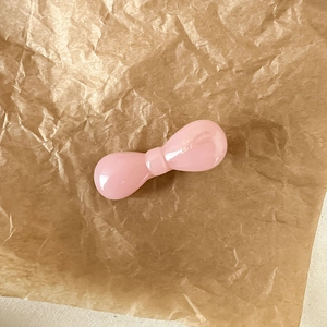 Gros plan d'une pince à cheveux rose clair avec texte doré sur papier vintage