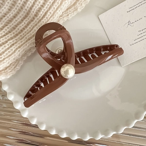 Elegante pinza per capelli marrone con perla bianca su sfondo beige accogliente