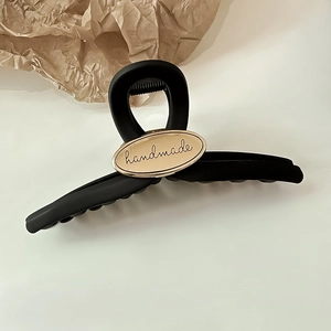 Macro view of large matte black hair claw clip with golden handmade engraved oval plate