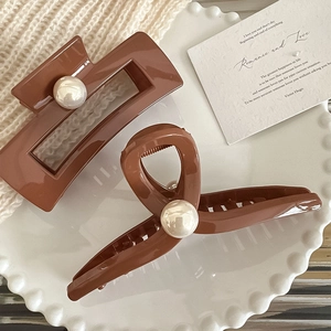 Dettaglio di eleganti mollettoni marroni con grandi perle su un vassoio di ceramica bianca
