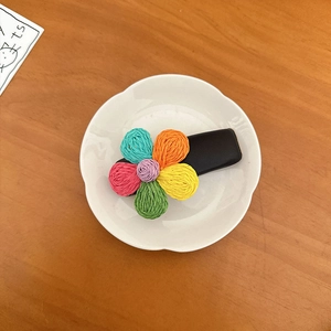 Dettaglio di un fermaglio per capelli a fiore intrecciato con petali colorati su pelle