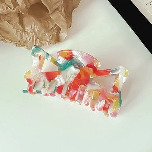 Colorful marbled acetate bow claw clip for hair styling on minimalist desk background