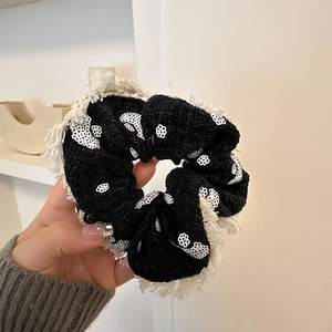 Gros plan d'un chouchou en tweed vintage avec fleurs à paillettes blanches et franges