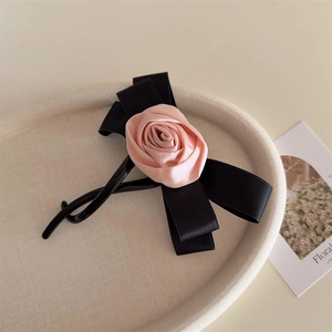 Haarklammer mit rosa Satinrose und schwarzer Schleife auf einem Tablett, elegantes Accessoire
