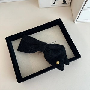 Detailed view of black textured fabric bow hair clip with decorative gold metal button