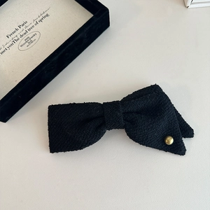 Detailed close-up of a black tweed bow hairclip with a vintage gold metal button accent