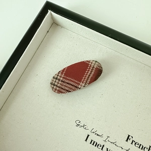 Detail view of oval hair clip with vintage red brown plaid fabric texture on canvas board