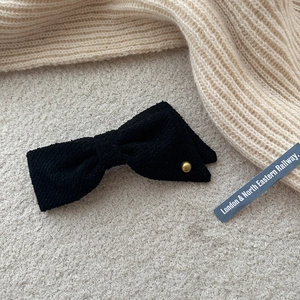Macro detail of black tweed bow hair clip with vintage gold button on cozy knit texture