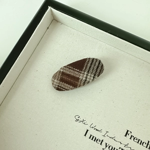Close-up of vintage brown plaid fabric oval hair clip on a minimalist display tray