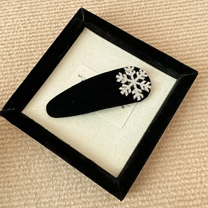 Detailed view of black velvet hair clip featuring a sparkling rhinestone snowflake decoration