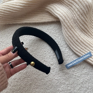 Close-up of black wool fabric headband with gold metal buckle and handmade label detail