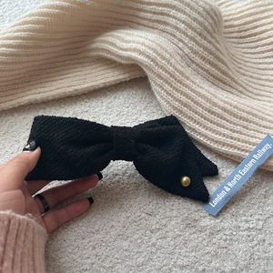 Close-up of black tweed bow hair clip with gold bead detail and textured fabric