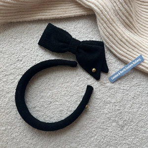 Elegant black tweed headband with asymmetric bow and gold button for a stylish hair look