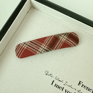 Close-up of vintage plaid fabric oval hair clip with red and brown tartan texture
