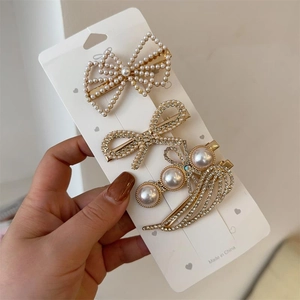 Lot de trois barrettes élégantes en perles et strass avec base dorée présentées sur carte