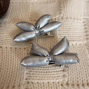 Paia di fermagli per capelli a fiocco 3D argento lucido su sfondo in maglia beige