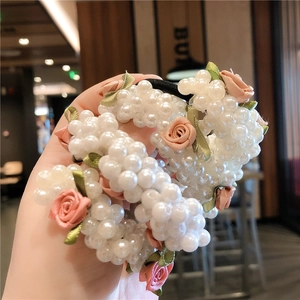 Vue détaillée d'un chouchou en perles blanches avec roses roses en tissu et feuilles