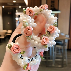 Détail d'un chouchou en perles avec rose en tissu rose et feuilles vertes tenu en main