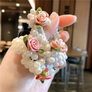 Détail du chouchou en perles avec roses en satin rose et feuilles vertes sur élastique noir