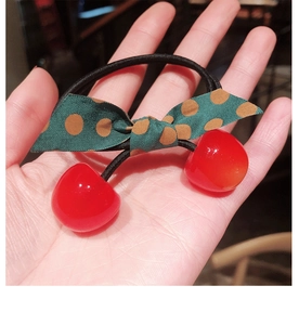 Detail of red resin cherry charms and polka dot bow on an elastic hair tie