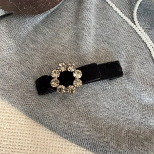 Macro shot of black velvet hair clip featuring eight sparkling grey rhinestones on grey fabric